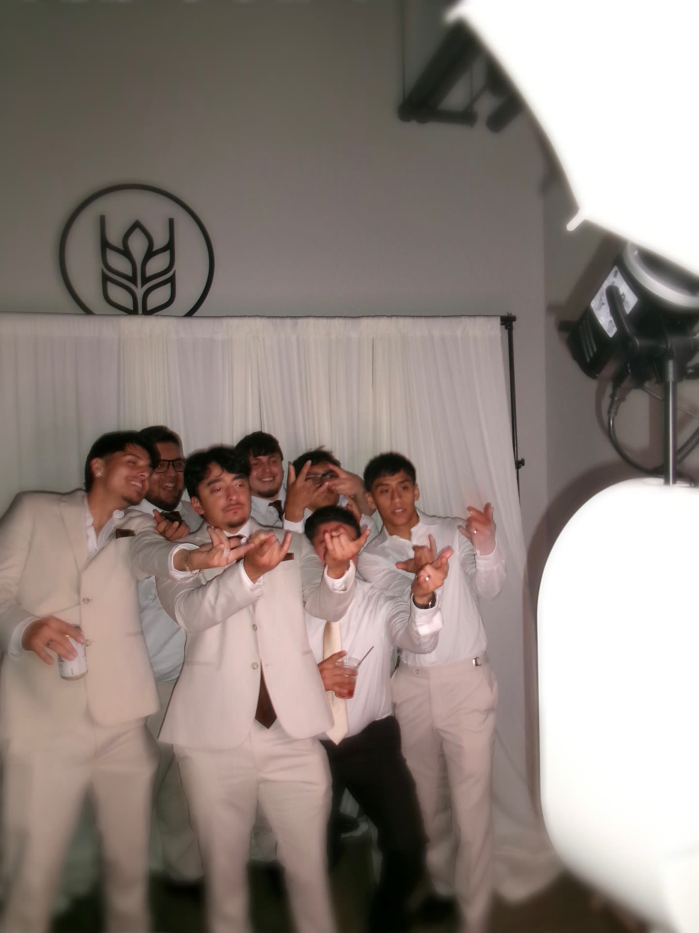Groomsmen in cream suits posing together in front of the Memento photo booth backdrop