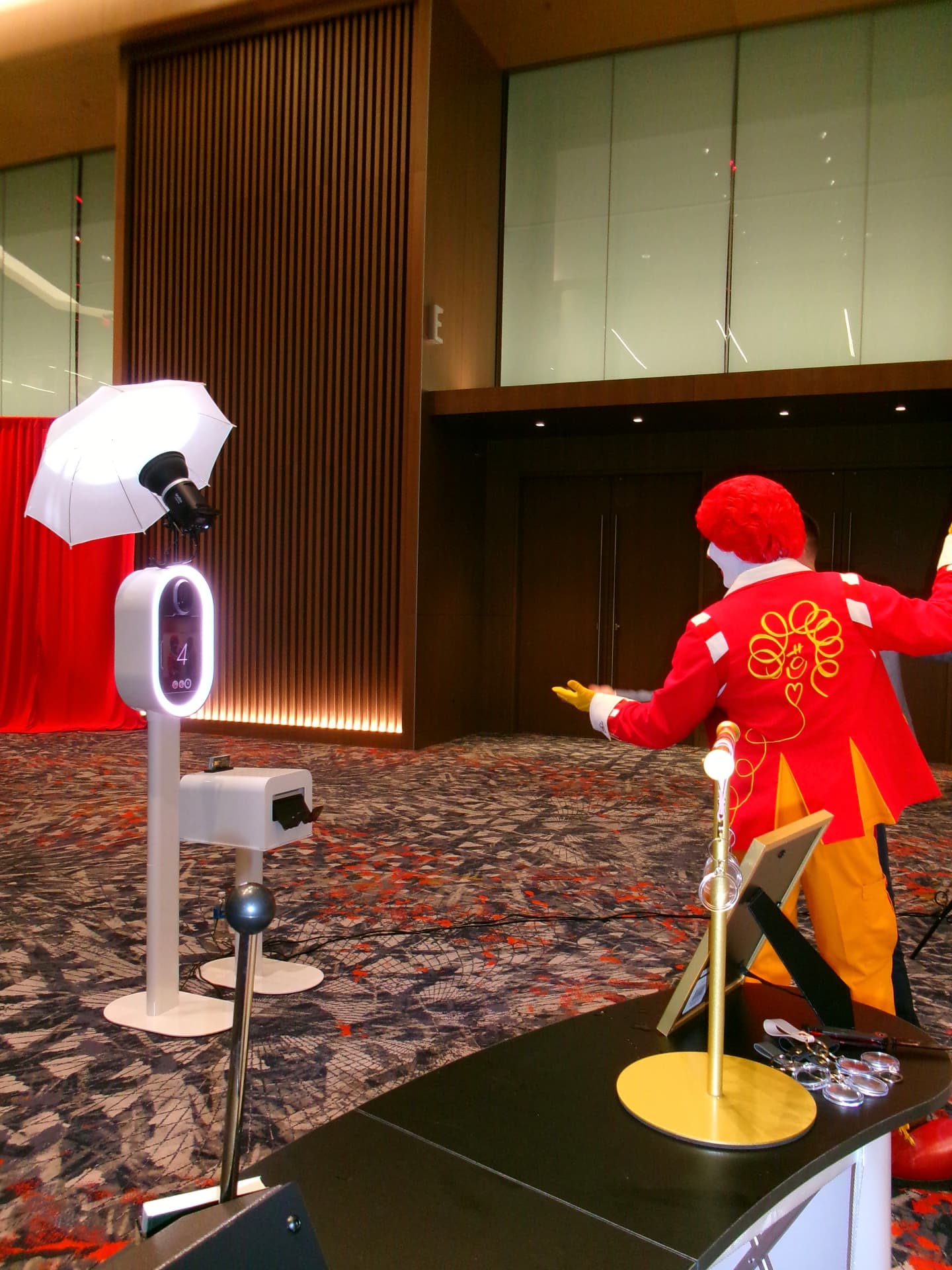 A guest in a red and yellow costume posing in front of the Memento photo booth, with its ring light and umbrella flash, in a wood-paneled ballroom