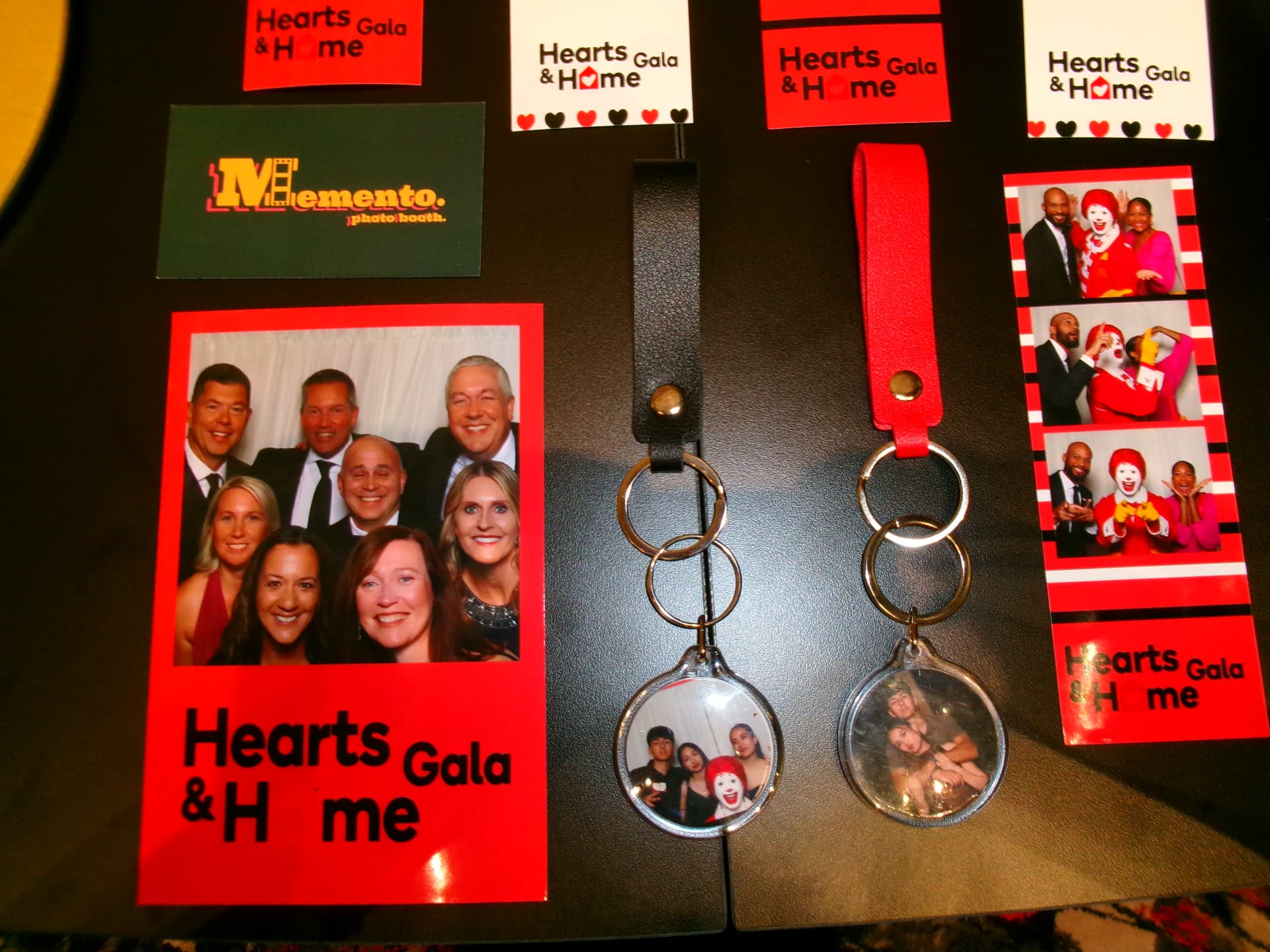 Memento keepsakes on a table — a group photo card, two photo keychains with leather straps, a photo strip, and a Memento card