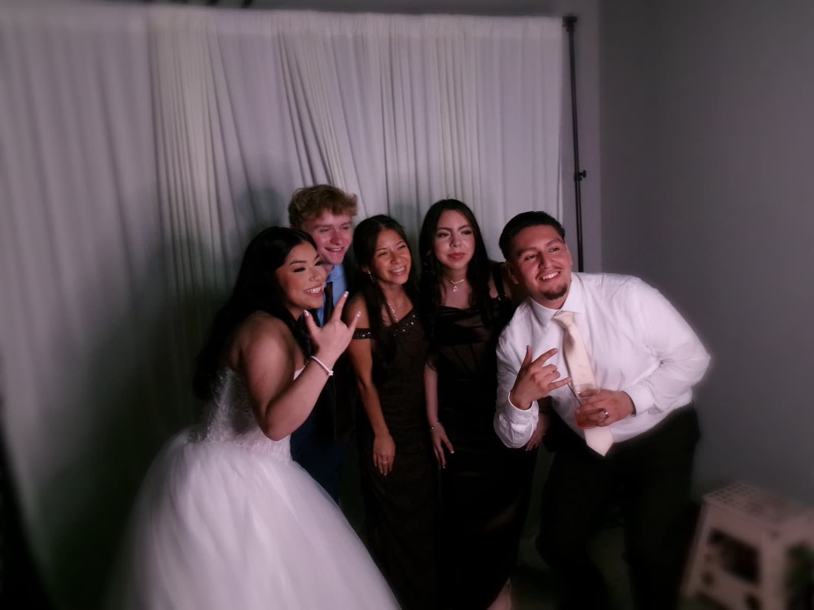 A bride and her friends posing together in front of a white draped backdrop in the Memento photo booth